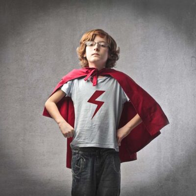 Young boy dressed as a superhero with a red cape and lightning bolt shirt.