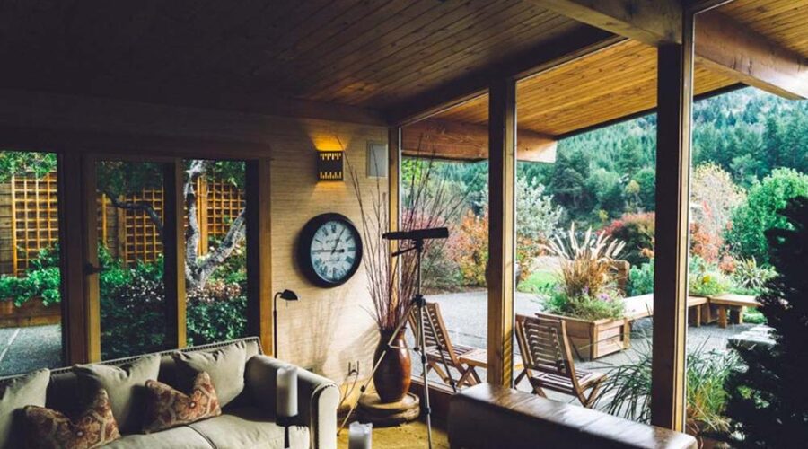 Cozy indoor living space opening to a lush garden patio with wooden ceiling and large windows.