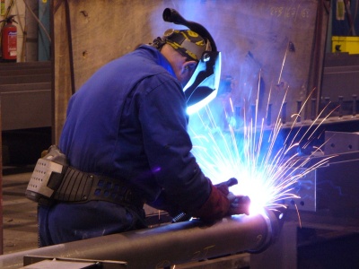 Welder in protective gear sparks bright arc while working on metal.